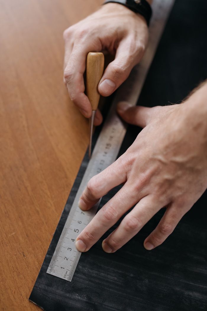 Detailed shot of hands working with chisel and ruler on a black surface for precise marking.